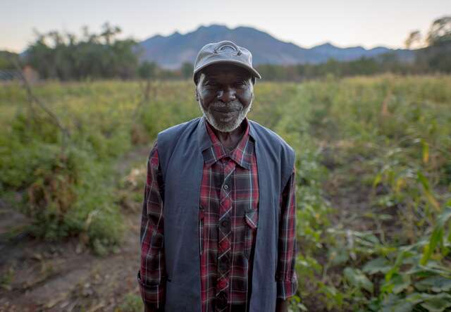 A man smiling into the camera standing in front of a field