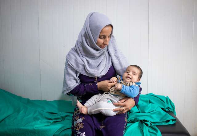 En mamma håller sitt spädbarn i famnen på en RESCUE:s hälsocenter i Syrien.