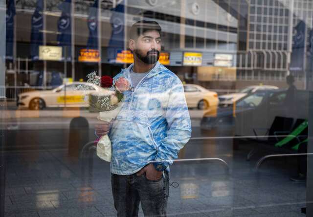 Der junge Mehdi wartet mit einem Blumenstrauß vor dem Flughafen auf seinen Bruder und schaut zur Seite.