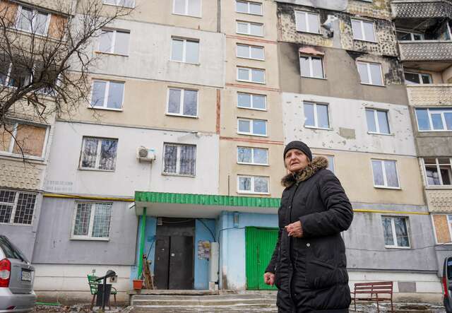 Kateryna stands in front of her apartment in Ukraine, which shows shelling damage