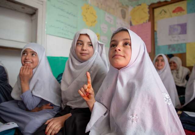 Students raise their hands to answer questions at an IRC led community based education session in Afghanistan.