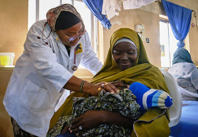 En läkare undersöker ett spädbarn som ligger i sin mammas knä.