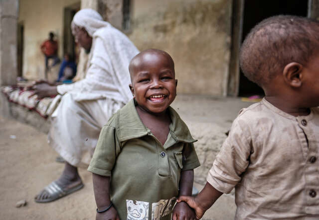 En pojke står och ler och håller sin bror i handen.