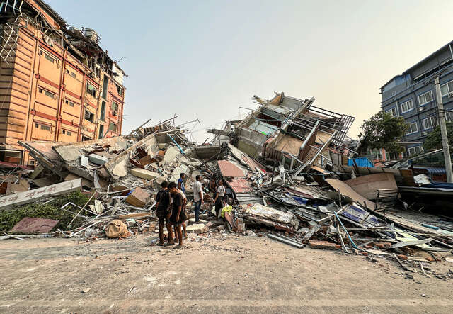 Människor i Myanmar står vid rasmassorna av en kollapsad byggnad efter en jordbävning.