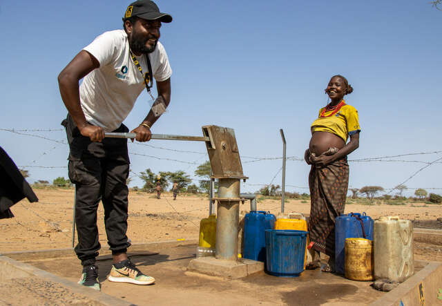 En man pumpar vatten vid en vattenstation i Etiopien, bredvid honom står en gravid kvinna med vattendunkar.