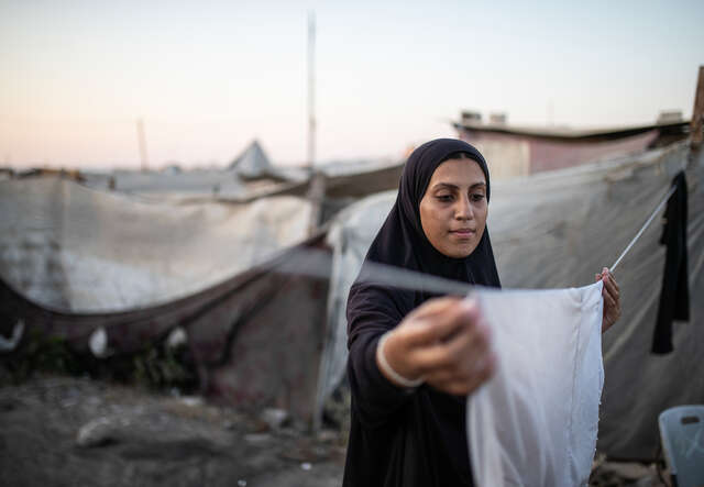En flicka i Gaza hänger tvätt utanför ett tält.