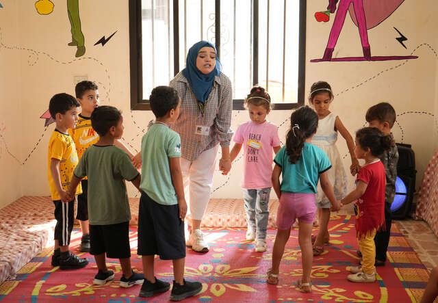 En grupp barn står i en cirkel tillsammans med en ledare i ett ljust rum i Libanon där RESCUE är verksamma för att ge yngre barn stöd.