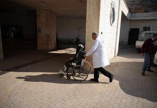 Nurse Yousef*, 53, pulls Huda*'s wheelchair, 25, entering her into the emergency department at “Al-Maghara" Hospital in Atarib, western Aleppo countryside, northwestern Syria to change the dressing on her broken leg.