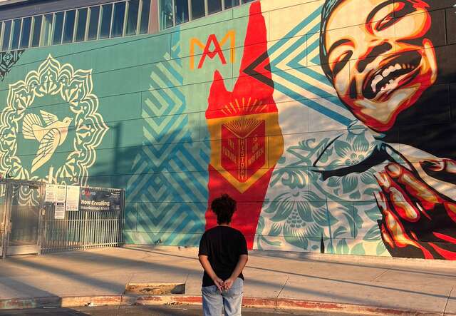 M stands in front of a mural, admiring the art.