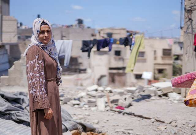 A Palestinian woman walks through the remains of a destroyed building.