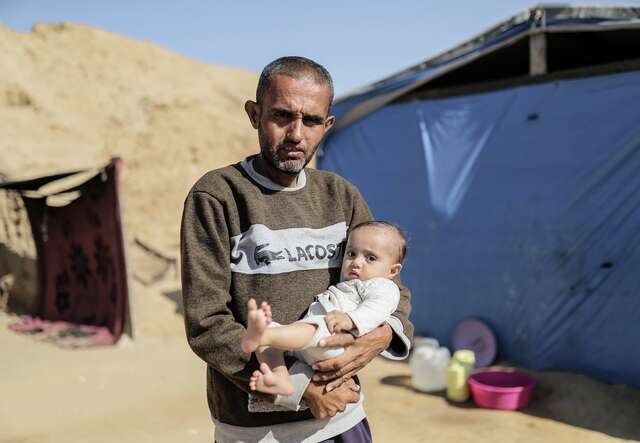 A Palestinian father holds his young, malnourished daughter in his arms.