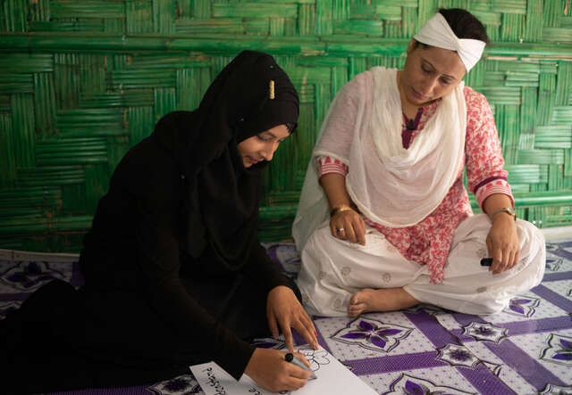 A female teacher sits next to a female student an IRC safe space in Bangladesh.