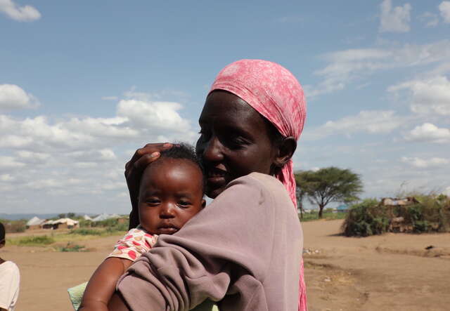 한 엄마가 아기를 소중히 안고 볼을 대며 미소 짓고 있습니다.