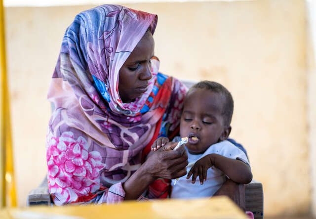 Hawaya feeds Wayel a malnutrition biscuit.