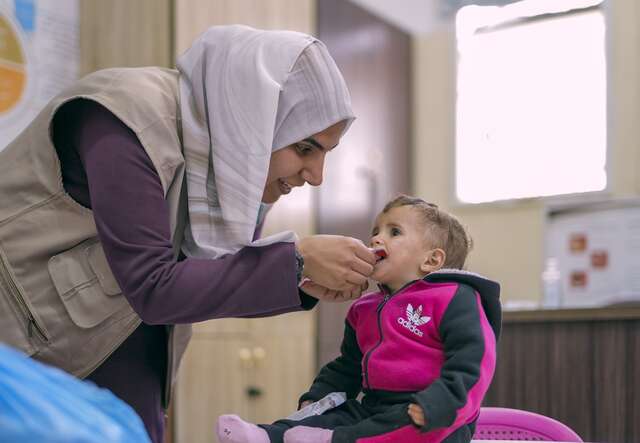 A woman in a hijab feeding a young boy wearing a pink jacket