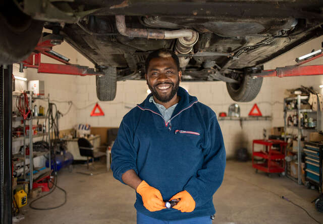 Florent stands in the car workshop, smiling at the camera