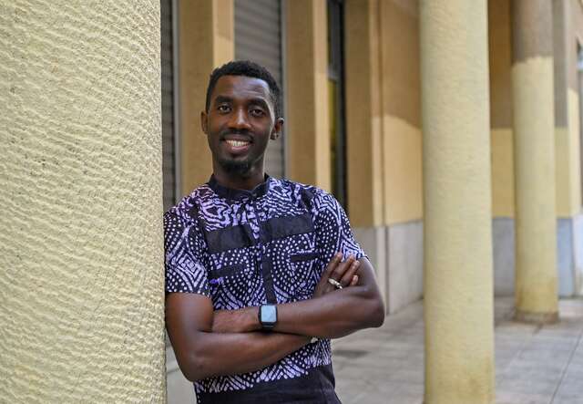 Moussa leans against a wall, smiling at the camera.