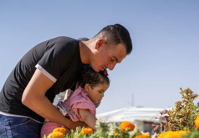A father holds his young daughter as they walk through a garden.
