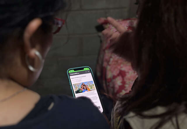 Two women look at a phone screen, we see them from the back.