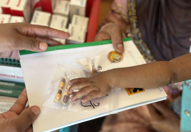 Two adults are holding a file with pills on top of it. The yound child's hand is touching the pills.