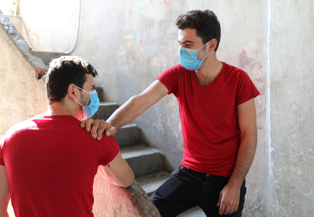 Two brothers wearing red and face masks look at each other.