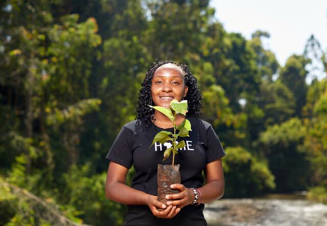 Elizabeth Wathuti looks at the camera and holds a vase with flowers outside in nature scenery