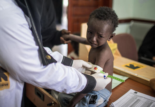 A health worker at an IRC-supported clinic in Sana'a, Yemen, measures a young boy's arm to confirm he is suffering from malnutrition.