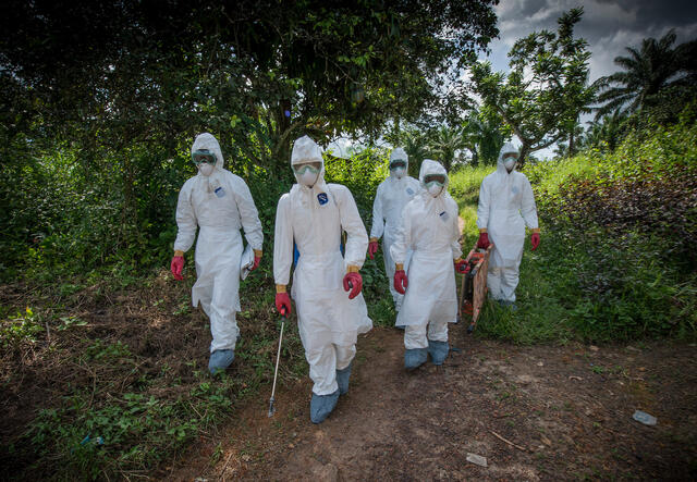 Five people walking wearing hazmat suits.
