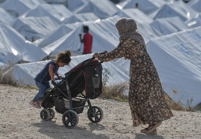 A 33-year-old Syrian refugee, wearing a face mask to protect herself from the coronavirus, pushes two of her children in a stroller past rows of tents in a crowded refugee camp on the Greek island of Lesbos.