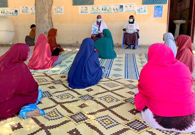 Two health workers in masks speak to a group of women about the coronavirus in a health clinic in Mogadishu, Somalia.