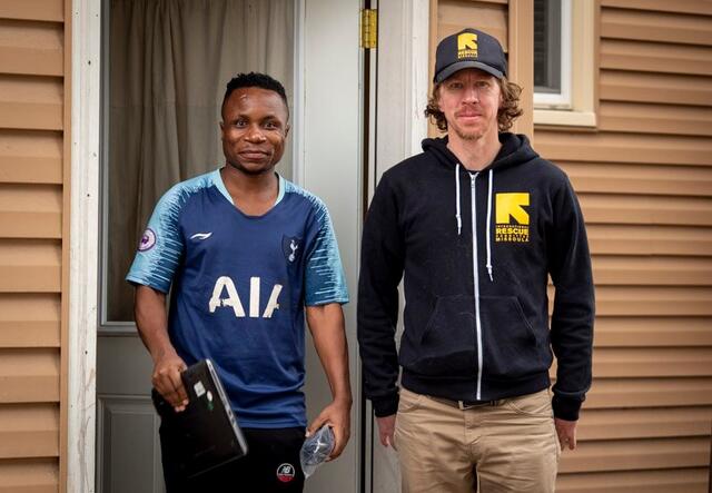 An IRC staff member stands next to an IRC client holding a laptop.