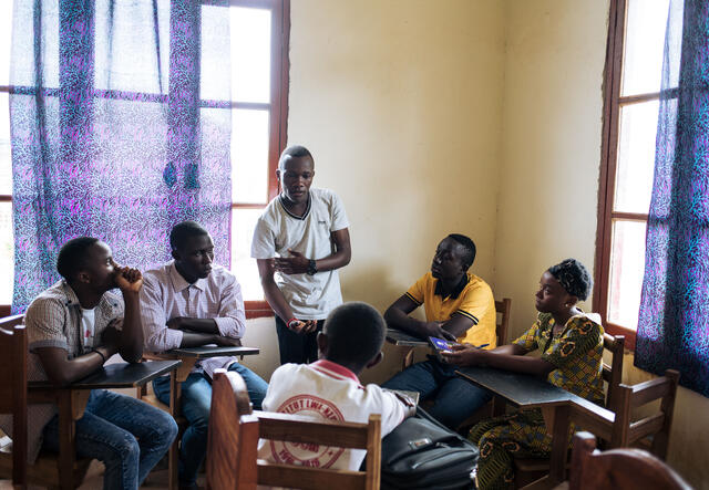 Benjamin, standing in a classroom in Congo, speaks to other teenagers seated at desks around him about Ebola.