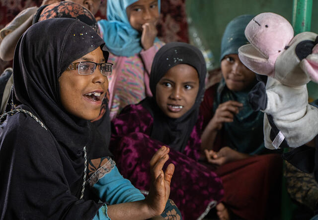 A young girl talks to a cow puppet as other children watch