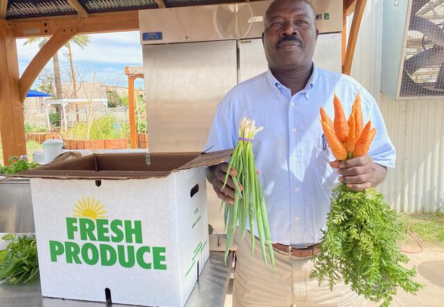 A man shows carrots and green onions that he grows and sells.