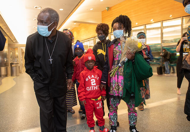 Patrice, Mauwa and family after they arrived at the airport stand in the airport. Mauwa is holdin g
