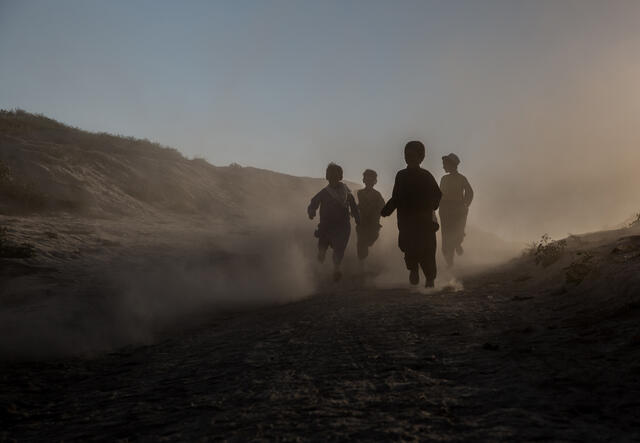 Children run through a desert and mountain landscape. The light is such that their faces are obscured.