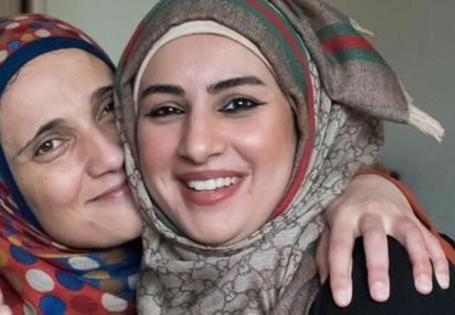 Two women from Afghanistan are smiling as they have their heads nestled against each other.