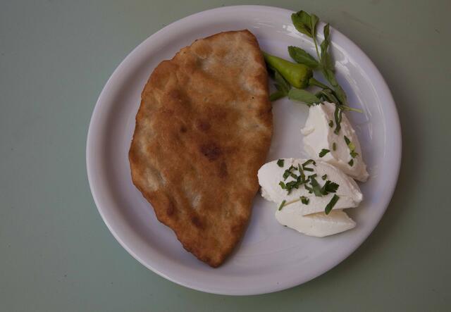 A dish of Afghan Bolani on a grey table. The dish consists of a fried piece of dough made of flour and potatoes, cheese and green herbs.