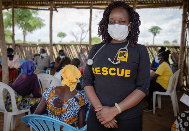 Dr. Ruth Grace Babirye stands wearing a protective face mask as elderly people  sit in an open waiting room in Bidi Bidi refugee settlement in Uganda to get vaccinated against COVID-19.