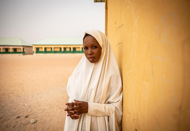 A young woman leans against the wall of a school building.
