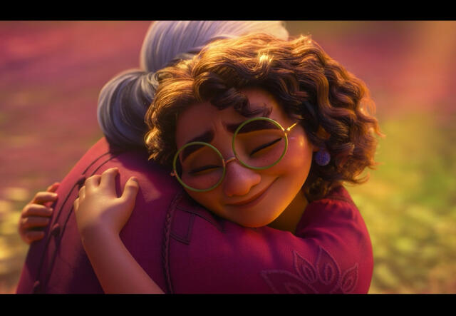 A screenshot from Disney's animated film Encanto. Mirabel, who has curly hair and wears glasses, hugs her Abuela, who has grey hair in a bun and a pink shirt.