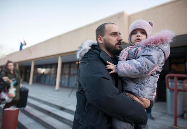 Dressed in winter jackets, a man holds his young daughter at a train station in Poland.