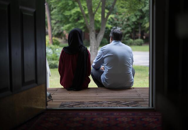 In a doorway to a home, a couple sits on a stoop and looks away from the camera.