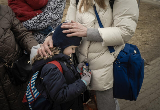 A close up of a young girl leaning against her mother, who places her hands on her back and head.