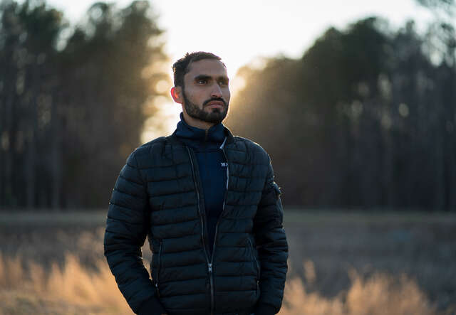 Photojournalist Mohammad Anwar Danishyar stands in front of a forest in the evening.