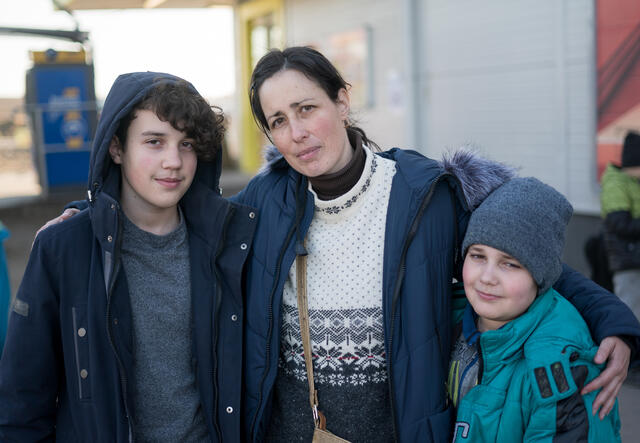 A woman looks at the camera with her arms around her two sons. All are wearing winter clothes.