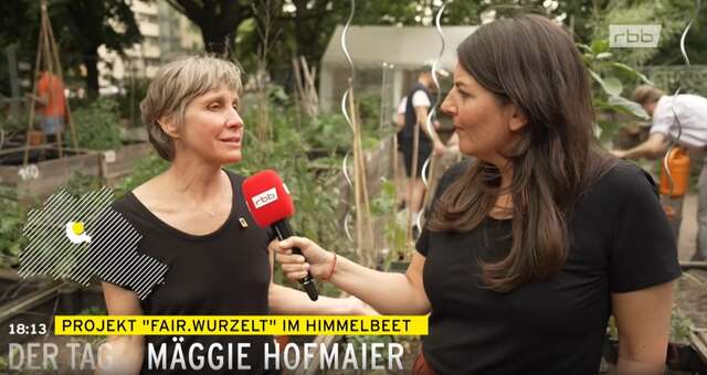 Eine Frau mit kurzen grauen Haaren wird mit einem roten Mikrofon in einem Außengarten über das Projekt Fair.Wurzelt im Himmelbeet interviewt,