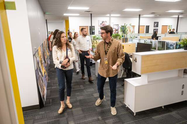 A small group walks through the well lit IRC office space passing by cubicles on a tour during the Open House.