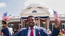 A man holds small American flags in each hand at a naturalization ceremony for new American citizens.