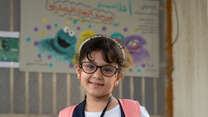 A girl in glasses poses for a photo in an IRC classroom in Iraq.
